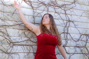 Student poses in red dress in front of vines